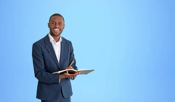 ノートとペンを保持し 青い壁の近くに立ってエレガントなスーツで陽気な若いアフリカ系アメリカ人ビジネスマンの肖像画 計画の概念 スペースのコピー — ストック写真