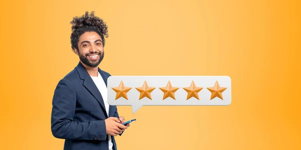 5つ星評価を与えるスマートフォンと陽気な若いアフリカ系アメリカ人ビジネスマンの肖像画 サービスランキングの概念 黄色の背景 — ストック写真