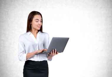 Resmi kıyafet giyen çekici bir iş kadını dizüstü bilgisayarını arka planda boş beton duvarın yanında tutuyor. Model kavramı, başarılı iş adamı, öğrenci, mobil aygıt
