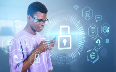 Siyah adam telefonu kullanıyor, gülümsüyor. Çeşitli dijital arayüz simgeleriyle parlayan kilit, hud hologram ve ikili daire. Gizlilik ve veri koruması kavramı