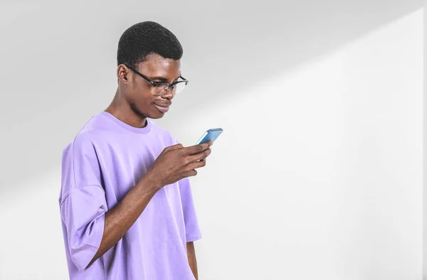 カジュアルを身に着けているアフリカ系アメリカ人ビジネスマンは 背景に白い空の壁の近くにスマートフォンを保持立っている 作業プロセスの概念 同僚のためのテキストメッセージ モバイルガジェット — ストック写真