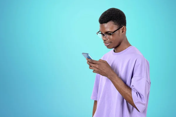 カジュアルな服装をしているアフリカ系アメリカ人ビジネスマンは 背景に鉄の空の壁の近くにスマートフォンを持って立っている 作業プロセスの概念 同僚のためのテキストメッセージ モバイルガジェット — ストック写真