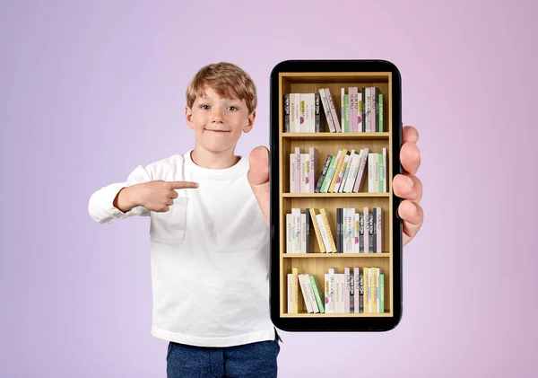 Young handsome boy wearing casual wear is showing smartphone case with digital library. Bookshelf with various books. Concept of e-learning and online education. Purple wall in background