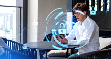 Ciddi genç Avrupalı iş adamı ofiste tablet bilgisayar kullanıyor ve çift katmanlı siber güvenlik arayüzü ve gezegen hologramı kullanıyor. Veri koruması kavramı
