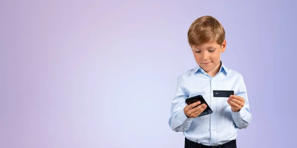 紫の背景の上に立ってスマートフォンやクレジットカードを保持正式な服で愛らしい男の子の肖像画 インターネットバンキングとオンラインショッピングの概念 スペースのコピー — ストック写真