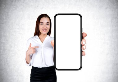 İş kadını büyük akıllı telefonu gösteriyor ve işaret ediyor. Fotokopi alanı görüntüsü, gri beton arka plan. Web sitesi ve mobil uygulama kavramı