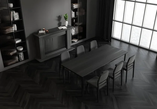 Top view of dark dining room interior with table and chairs, shelf with books and fireplace. Panoramic window on Singapore skyscrapers, black hardwood floor. 3D rendering