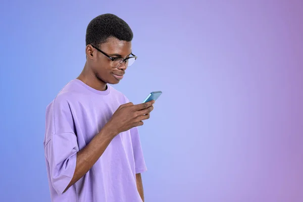 身穿休闲装的非裔美国商人站在紫色空墙旁边拿着智能手机 工作过程的概念 给同事 移动设备的短信 — 图库照片