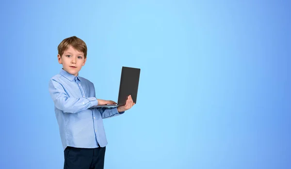 青い背景の上に立ってラップトップを保持する正式な服に集中した男の子の子供の肖像画 Eラーニングやソーシャルメディアの概念 現代の技術とインターネット接続 スペースのコピー — ストック写真
