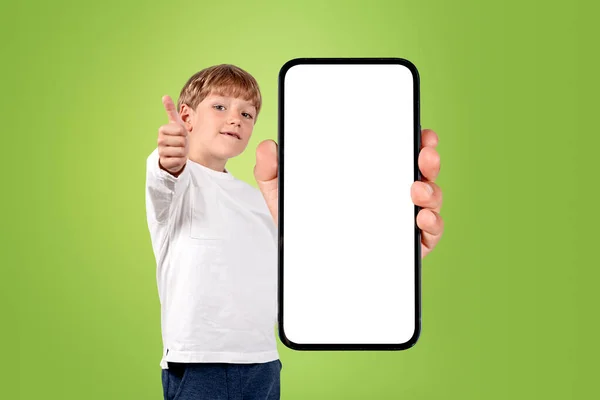 緑色の背景に大きなモックアップコピースペース画面で親指とスマートフォンを表示し 笑みを浮かべて子供の男の子 Eラーニングの概念 — ストック写真
