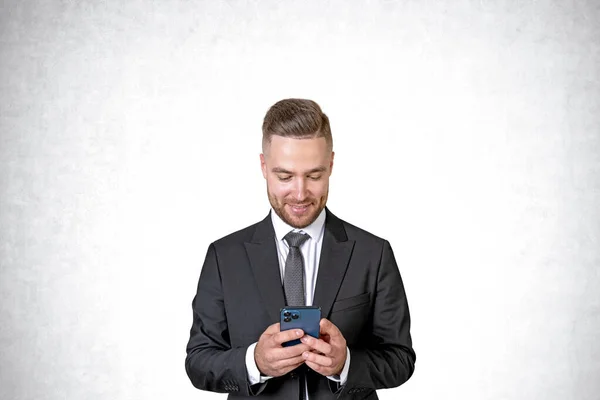 テキストメッセージを使用してオンラインで閲覧するビジネスマンを笑顔 黒の正式なスーツで成功した肖像画 コピースペース空のコンクリート壁の背景 ビジネスネットワークの概念 — ストック写真