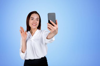 Telefonlu bir iş kadını, gülümsüyor ve mavi fotokopi arkaplanından görüntülü arama yapıyor. Çevrimiçi konferans ve ağ kavramı