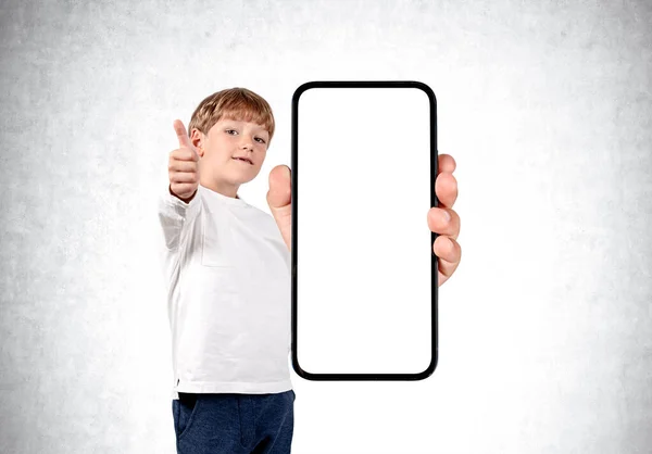 小男孩笑着肖像画 展示大拇指向上和智能手机与灰色混凝土背景的大型模拟屏幕 网上教育的概念 — 图库照片