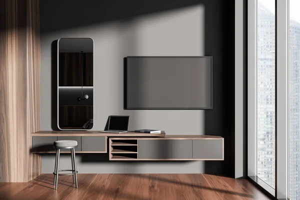 Dark living room interior with tv screen and dresser with laptop, stool and mirror. Workplace and panoramic window on skyscrapers view. 3D rendering