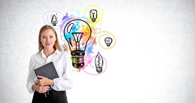 Elinde not defteri olan mutlu genç bir iş kadını, farklı renkte ampuller gri beton arka planda karalanıyor. Girişim ve fikir kavramı