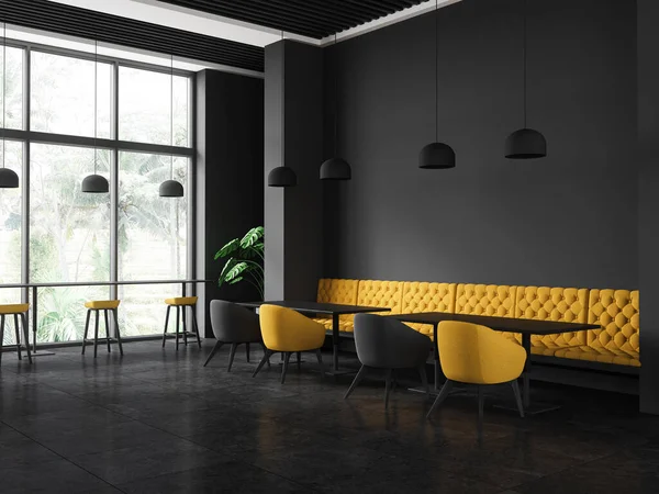 stock image Corner of stylish restaurant with dark gray walls, tiled floor, comfortable yellow sofa and colorful chairs standing near rectangular tables and long table with stools near window. 3d rendering