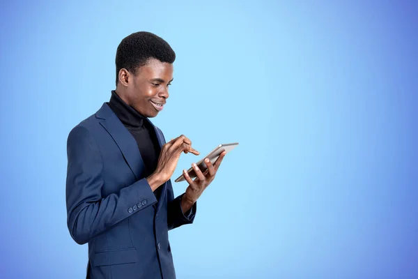 正式なスーツを着たハンサムなアフリカ系アメリカ人実業家が背景に空の青い壁の近くのタブレットデバイスで見て立っている 現代のガジェット モバイル通信 インターネット探検の概念 — ストック写真