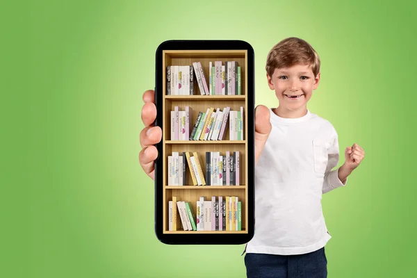 カジュアルウェアを着た若いハンサムな男の子は デジタルライブラリでスマートフォンケースを示しています さまざまな本がある本棚 Eラーニングとオンライン教育の概念 背景の緑の壁 — ストック写真
