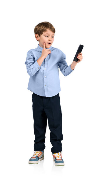 Boy kid holding phone with pensive look, finger to cheek, full length isolated over white background. Concept of online education and browse