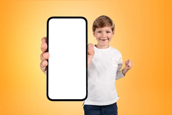 快乐的小男孩举起了拳头 拿着一个带有巨大模拟复制空间屏幕的智能手机 灰色的混凝土背景 成绩和研究的概念 — 图库照片