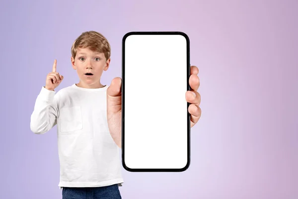 驚いた顔と指を指している男の子の子供は ライラックの背景に大きなモックアップコピースペース画面を持つ電話 募集及び取引の概念 — ストック写真
