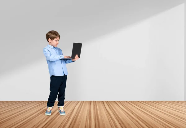 身穿正装的英俊小男孩站在空荡荡的白墙边 手里拿着笔记本电脑 木制硬木地板 现代小玩意的概念 进步的孩子 — 图库照片