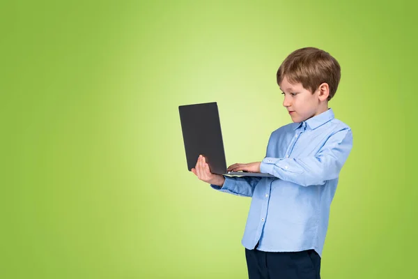 ノートパソコンを手に持って閲覧している子供の男の子 空のコピースペース緑の背景に肖像画 オンライン学習と学習の概念 — ストック写真