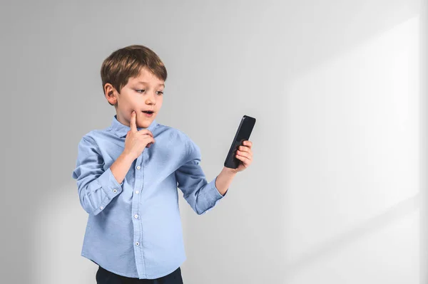 Шкільний Хлопчик Дивиться Телефон Пильним Виглядом Пальцем Щоку Порожньому Копіювальному — стокове фото
