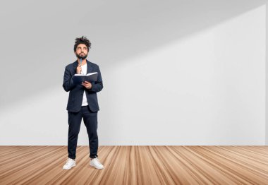 Resmi kıyafet giyen düşünceli Arap işadamı arka planda boş beyaz duvarın yanında duran bir defter tutuyor. Meşe ağacı ahşap zemin. Model kavramı, başarılı iş adamı, güven, bilgi