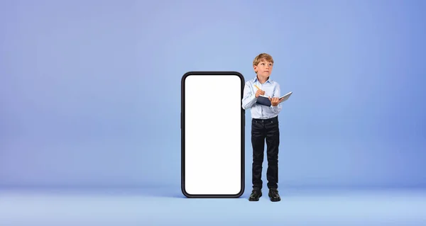 大きなスマートフォンの近くに立っている少年は コピースペース画面 青い背景をモックアップします メモを取って 調べる オンライン教育 Eラーニング ウェブサイトのコンセプト — ストック写真