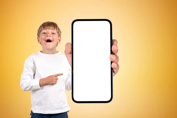 興奮した学校の少年は口を開き 大きなスマートフォンを指差して画面をモックアップし 黄色い背景 ソーシャルメディアと研究の概念 — ストック写真