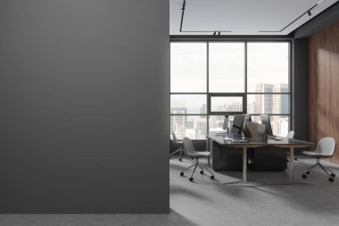 Gri ve koyu renkli ahşap duvarları, beton zemini, büyük bilgisayar tabloları olan modern açık uzay ofisinin içinde şehir manzarası olan pencerenin yanında duran ve solda duvar taklidi yapan. 3d oluşturma