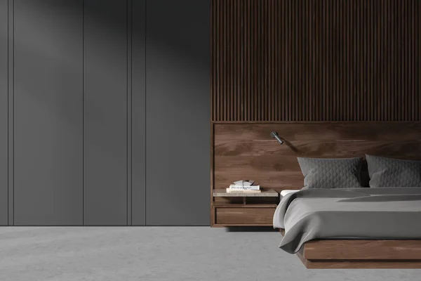 Dark home bedroom interior wooden bed on grey concrete floor. Cozy sleep room with minimalist furniture and nightstand with books. Copy space grey wall. 3D rendering