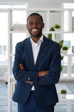 Resmi takım elbise giyen gülümseyen Afrikalı Amerikalı işadamı arka plandaki ofis işyerinde el ele poz veriyor. Model, iş adamı, zaman yönetimi, firma, şirket kavramı