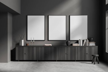 Karanlık oturma odasının içinde üç boş beyaz poster, şifonyer, dolap, çanak çömlek, kitap, mum, gri duvar, vazo var. Beton zemin. Minimalist tasarım kavramı. Model yap. 3d oluşturma