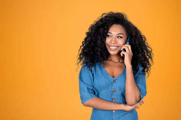 Black smiling woman calling on the phone, portrait on copy space yellow background. Concept of online connection and social media