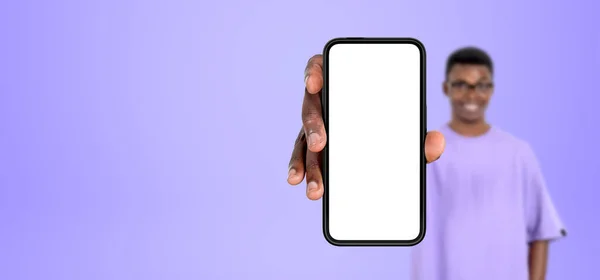 アフリカの若い男は コピースペース画面 空の紫色の背景をモックアップする大きなスマートフォンを示しています モバイルアプリ インターネット オンラインショッピングのコンセプト — ストック写真