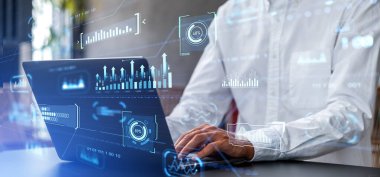 Bulanık ofiste dizüstü bilgisayar kullanan tanınmayan bir iş adamı grafiklerle çift taraflı dijital kontrol paneli kullanıyor. KPI ve dijital teknoloji kavramı, veri işleme