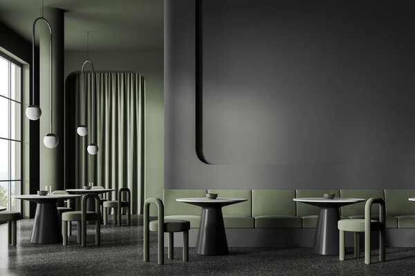 Interior of stylish restaurant with dark gray and green walls, concrete floor, round tables with chairs and cozy green sofa with copy space wall above it. 3d rendering