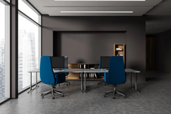 Dark work zone interior with pc computers and armchairs on desk, wooden shelf with decoration on grey concrete floor. Office workplace with panoramic window on Singapore skyscrapers. 3D rendering