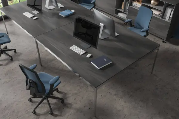 Top view of stylish office interior with concrete floor and massive dark wooden computer table with blue chair standing near it. 3d rendering
