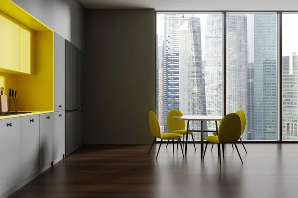 Interior of stylish kitchen with gray walls, wooden floor, cozy gray cabinets, yellow cupboards, big fridge and round dining table with yellow chairs standing near panoramic window. 3d rendering
