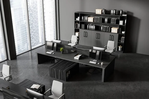 Top view of dark office interior with pc computers on desk in row, shelf with folders. Stylish workspace with minimalist furniture and panoramic window on skyscrapers. 3D rendering