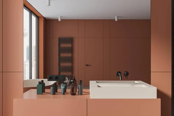 Interior of stylish bathroom with orange walls, elegant white sink standing on orange countertop with creams and toiletries and big mirror hanging above it. 3d rendering