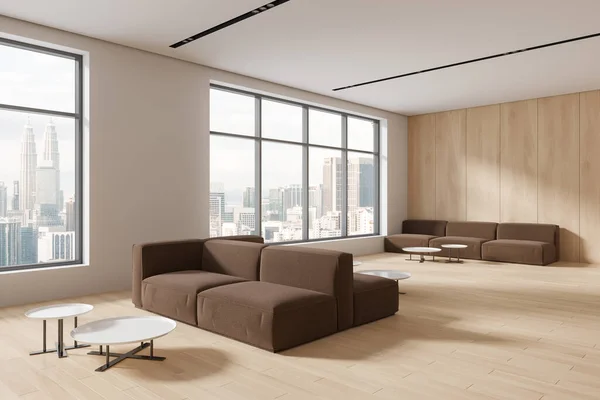 Stylish office wooden lounge zone interior with brown sofa and coffee table, side view furniture in row on hardwood floor. Panoramic window on Kuala Lumpur skyscrapers. 3D rendering