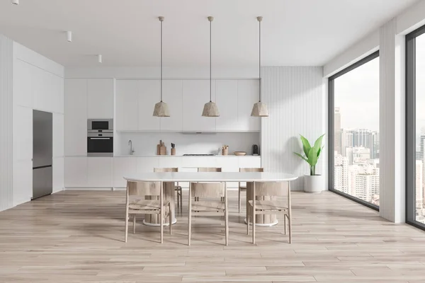 Interior of modern kitchen with white walls, wooden floor, comfortable white cupboards and cabinets with built in sink and cooker and long oval dining table with wooden chairs. 3d rendering