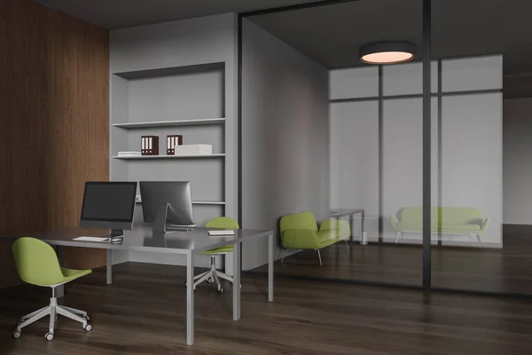 Interior of modern office with gray and wooden walls, dark wooden floor, two gray computer tables with green chairs and lounge area with two green sofas behind glass wall. 3d rendering