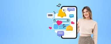 Mutlu, gülümseyen bir kadın fotokopi masalı arka planında model ekranlı, çeşitli dijital dünya simgeleriyle telefonu gösteriyor. Sosyal medya, iletişim ve haberci kavramı