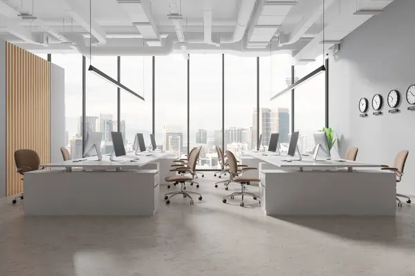 Interior of modern open space office with gray and wooden walls, concrete floor, white computer desks with beige chairs standing near panoramic window and clocks showing world time. 3d rendering