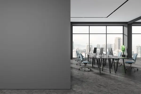 Dark office interior with pc computers, coworking space with armchairs and desk on grey concrete floor. Workspace and panoramic window on Kuala Lumpur. Mockup copy space wall. 3D rendering
